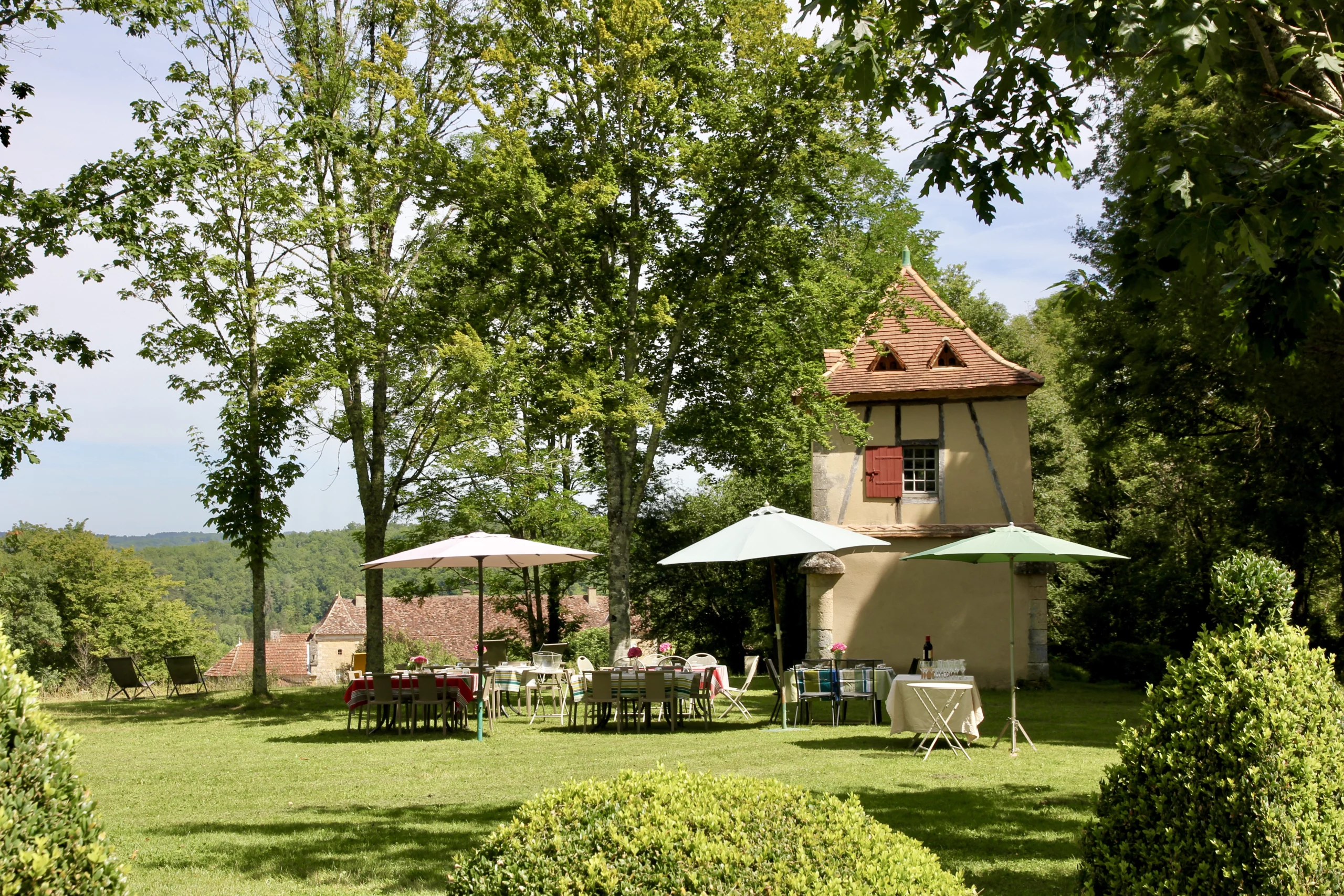 Jardin arboré du Château Terre Vieille avec pigeonnier, tables et parasols pour une dégustation en plein air.