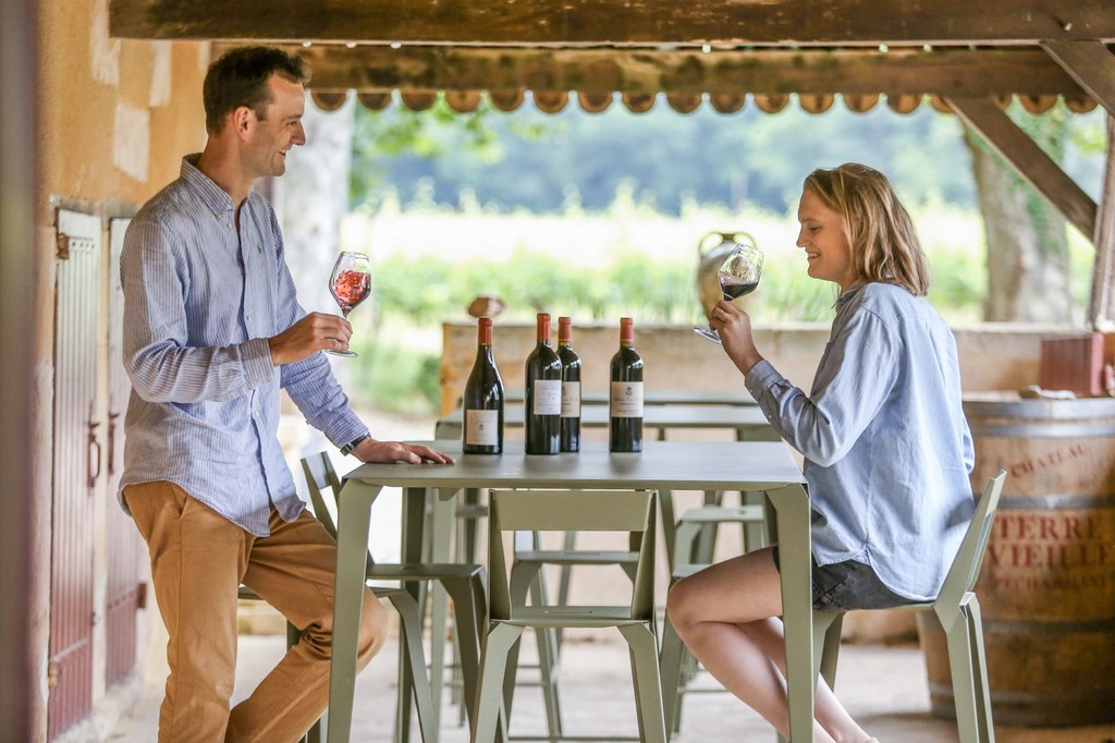 Deux personnes dégustent du vin sous un cabanon en pierre avec des vignes en arrière-plan, au cœur du vignoble de Pécharmant au Château Terre Vieille.